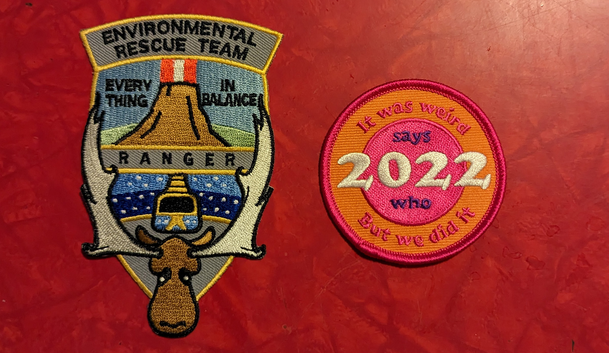 two patches I designed, one is a patch for the Environmental Rescue Team from the book The Terraformers, and the other is a 2022 survival badge for Says Who Podcast that reads It was weird, but we did it.
